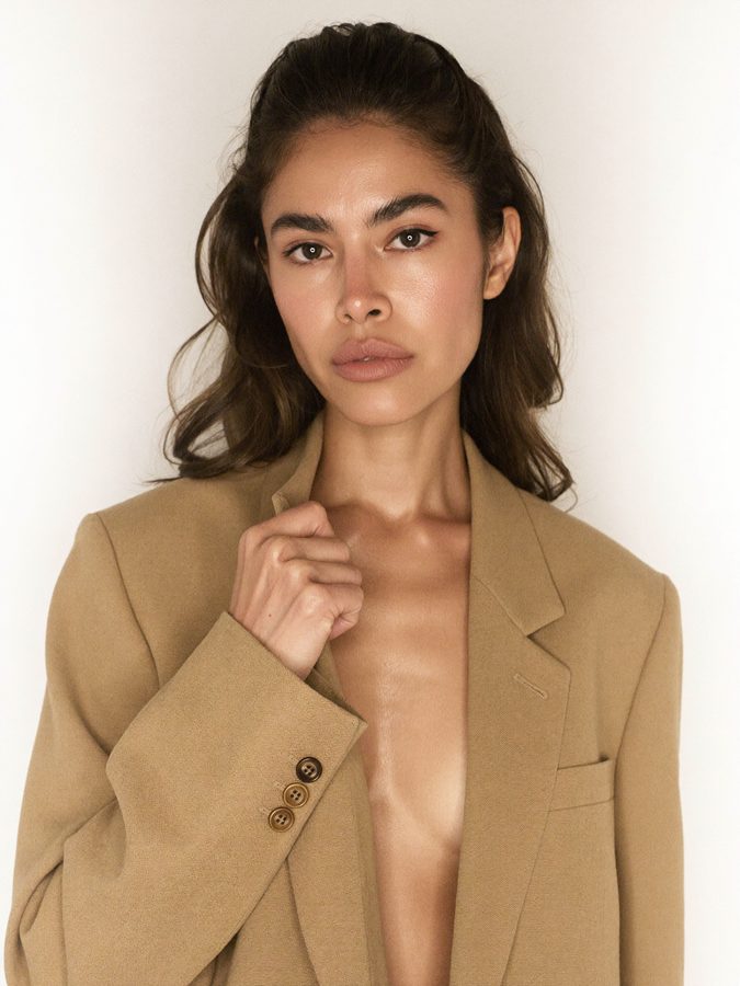Variation: the AI brand model turned three-quarters to camera right with her eyes back to the lens, camel blazer, white backdrop
