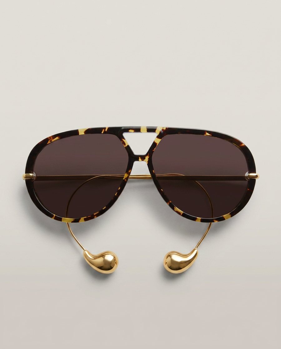 Oversized tortoiseshell and gold aviator sunglasses photographed flat and straight on against a soft pale studio backdrop