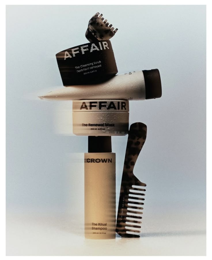 Haircare bottles, jars and a tube balanced in a vertical stack with a comb and hair clip.