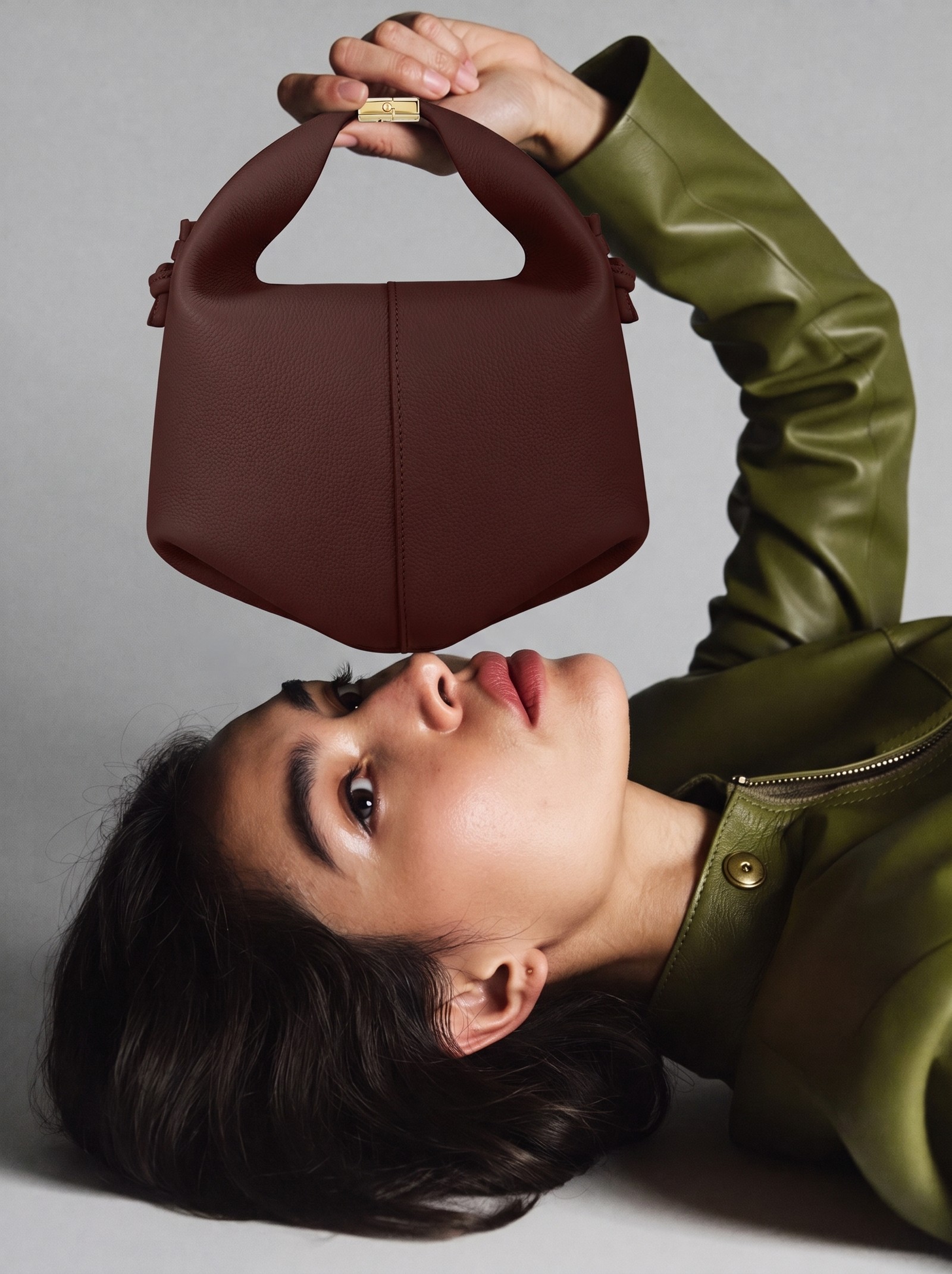 AI model in a half-body editorial pose, holding the burgundy top-handle bag against a neutral background