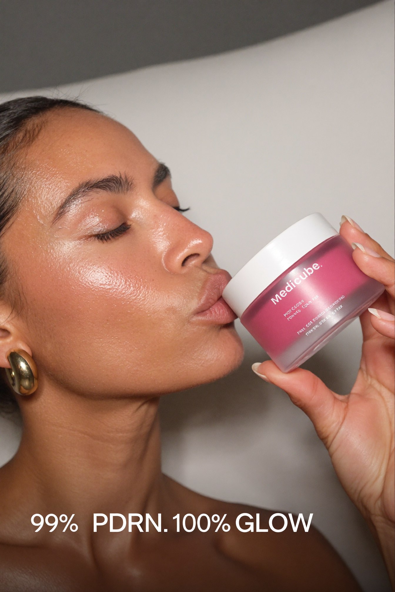 Vertical Pinterest pin, extreme close-up beauty editorial shot of a woman in side profile kissing the side of a pink skincare jar, bold text overlay reading 99 percent PDRN, 100 percent glow