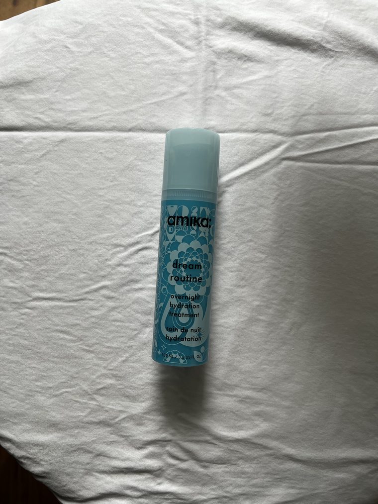 A light blue haircare bottle lying on a white cotton bedsheet, photographed from above in window light