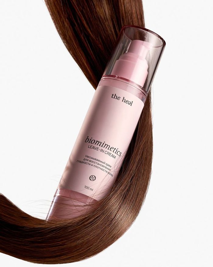 Reference image of a pink pump bottle resting on a curve of glossy dark brown hair against a white background