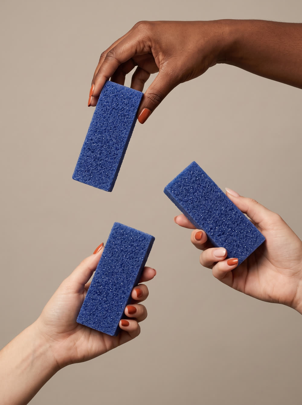 Product Shot still of three different hands holding the foot file against a warm neutral background