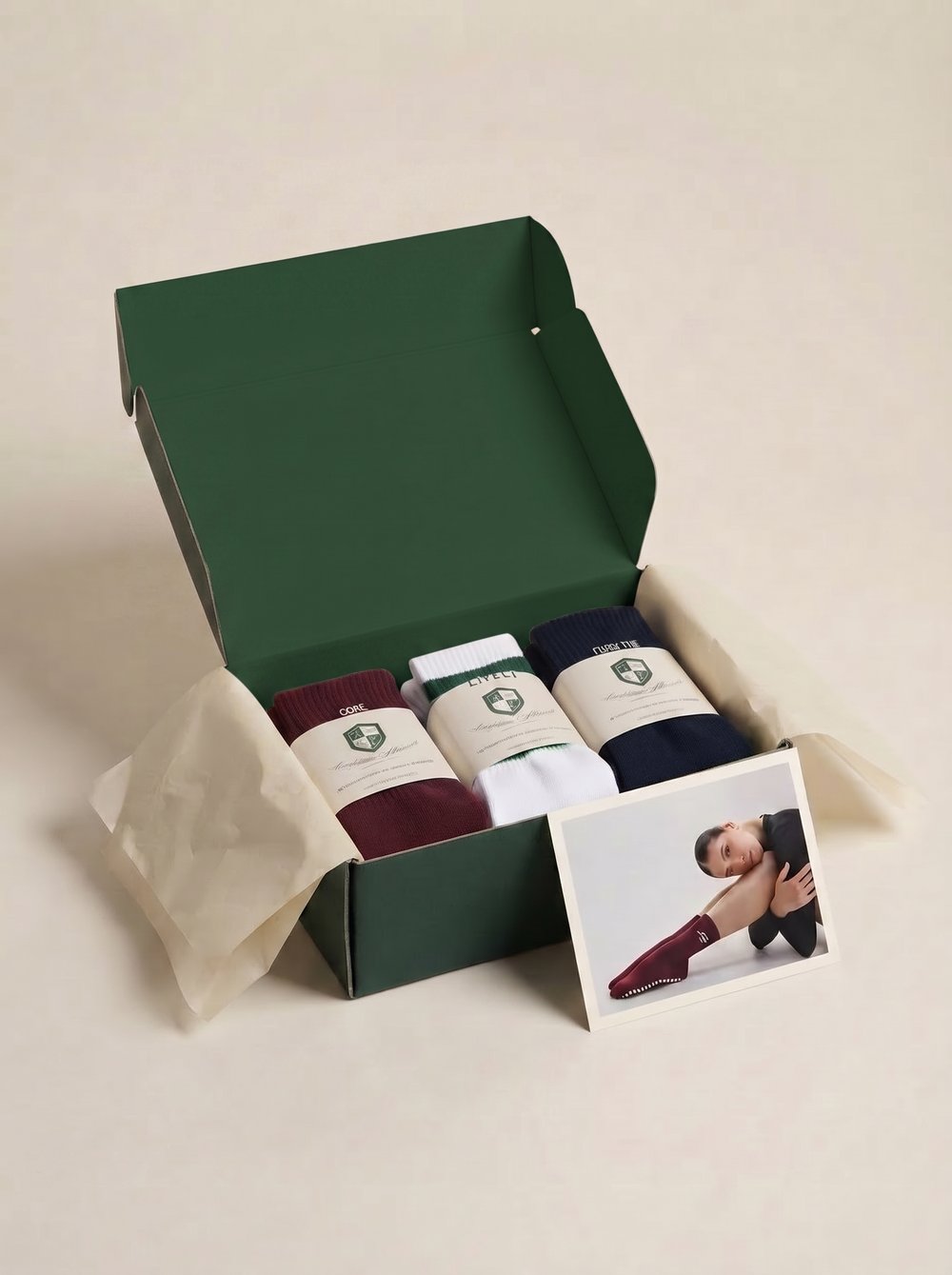 Same green gift box shown open, lid lifted, three folded and banded sock pairs visible inside on tissue paper