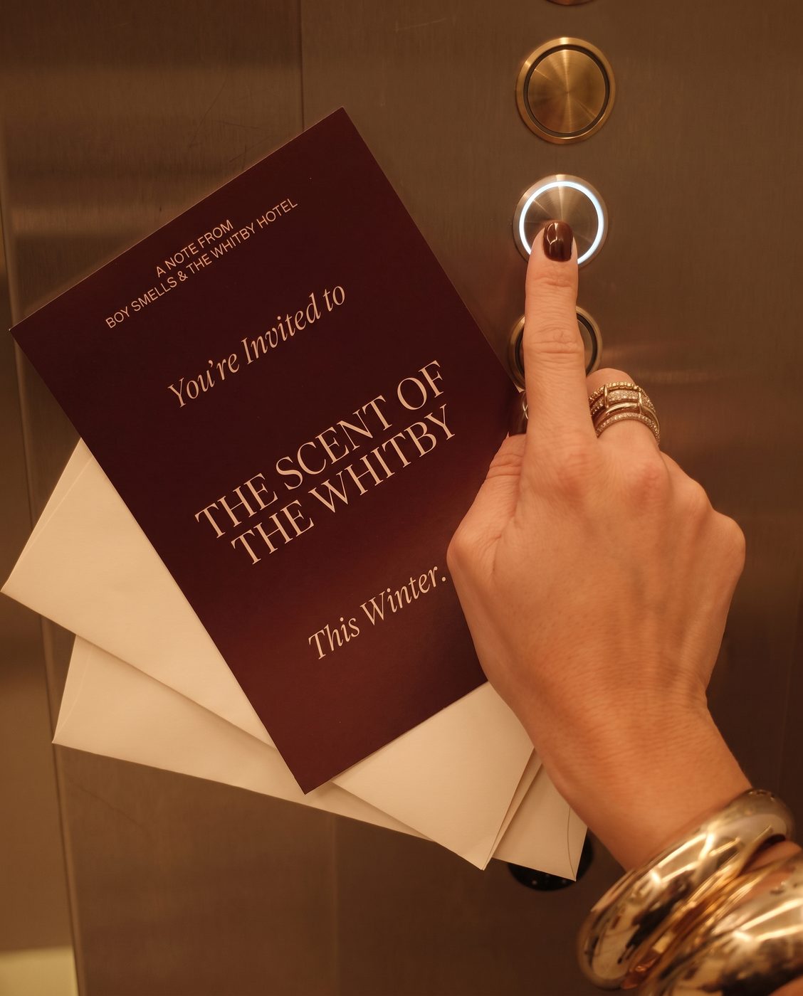 Instagram launch tile showing an invitation card reading You're Invited to The Scent of the Whitby This Winter, held up beside an elevator call button