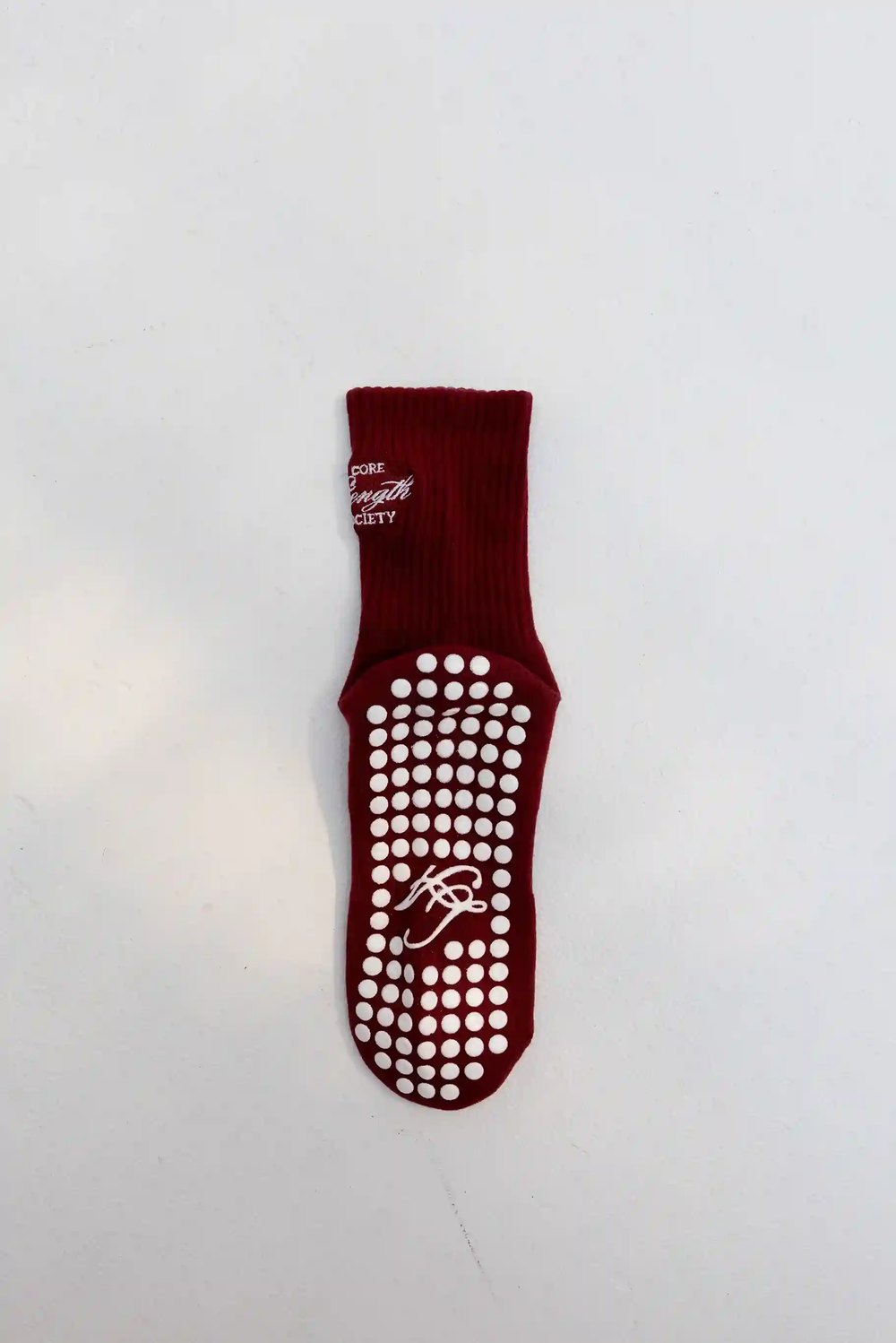 Phone photograph of the underside of a burgundy grip sock showing white silicone dots and a script monogram