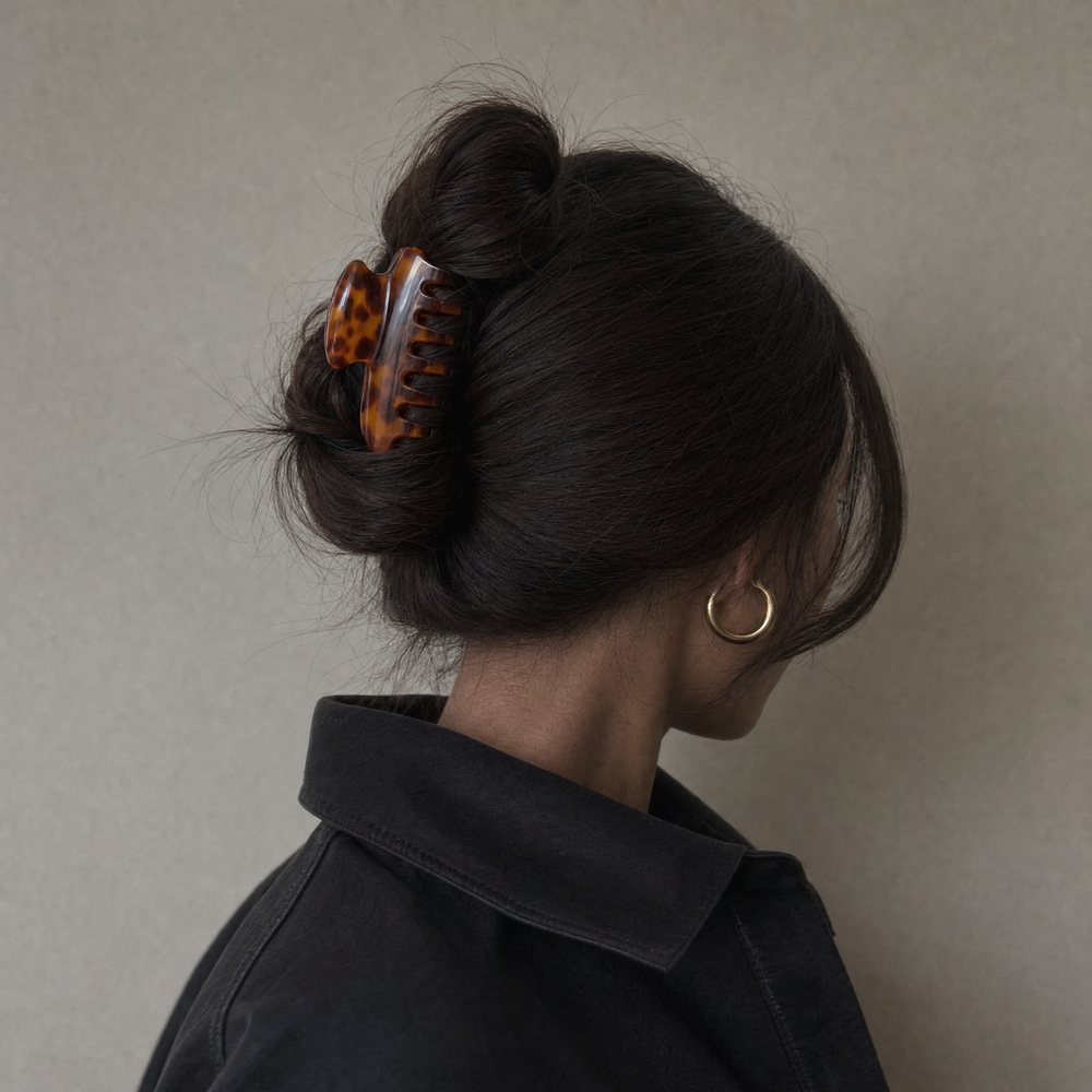 A tortoiseshell claw clip holding a dark messy bun, photographed from behind against a gray wall