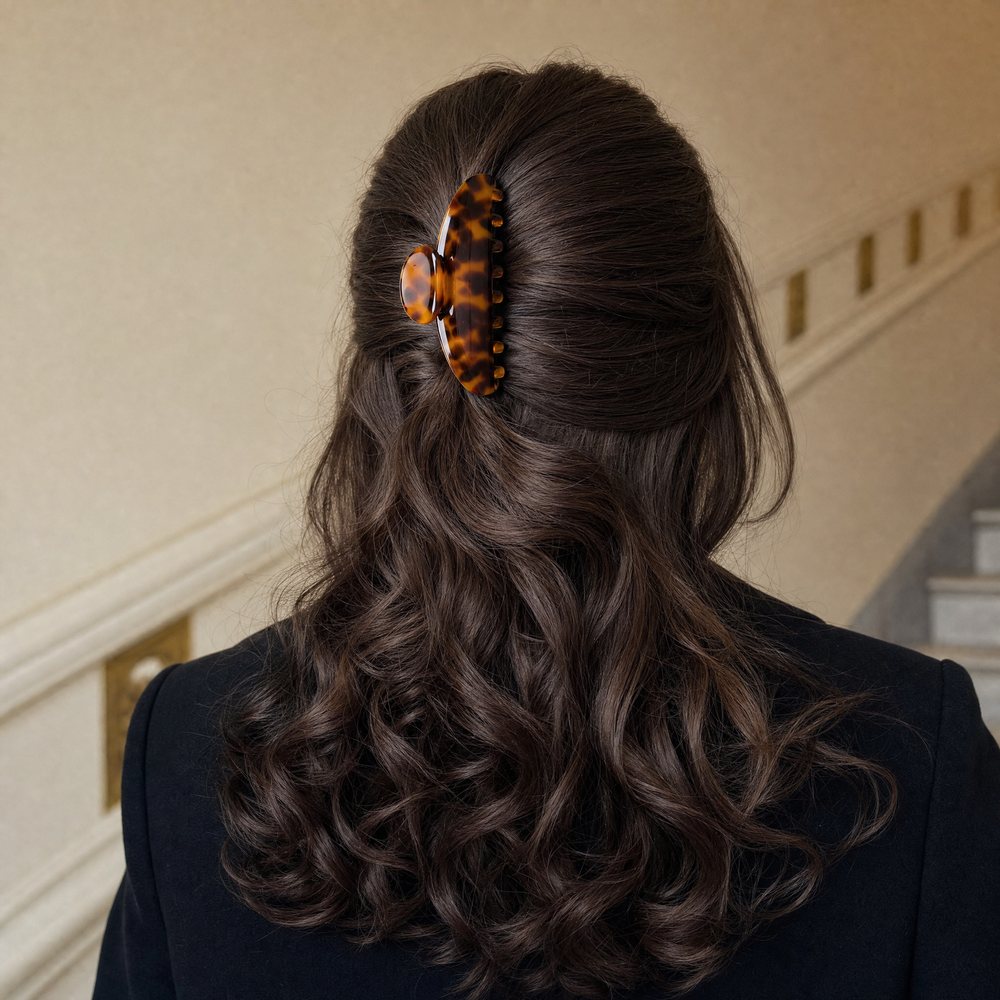 A woman from behind with a nineties blowout, a tortoiseshell claw clip holding the top section vertically, in a cream stairwell